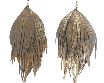 May include: A pair of long, gray and gold fringe earrings. The earrings are made of leather and have a sparkly finish.