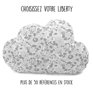 May include: A grey cloud-shaped cushion with a white background and a floral pattern. The text "CHOISISSEZ VOTRE LIBERTY" is above the cushion and the text "PLUS DE 50 RÉFÉRENCES EN STOCK" is below the cushion.