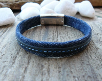 May include: A blue denim bracelet with a black leather trim and a silver magnetic clasp.