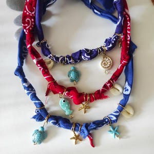 Op de afbeelding: Drie handgemaakte bandana-kettingen in rood-blauwe paisley-patronen. Elke ketting heeft goudkleurige ringen en bedels, waaronder zeeschildpadden, zeesterren en een vis. Schelpen zijn ook inbegrepen.