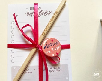 May include: A pink and white button with the text "Maitresse au TOP" and stars. A wooden pencil with the text "J'AI TOUJOURS BONNE MINE" is tied to a white notepad with a pink ribbon.