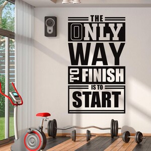 May include: A motivational wall decal in a gym setting. The black text reads "THE ONLY WAY TO FINISH IS TO START." An exercise bike, weights, and a speaker are also visible.