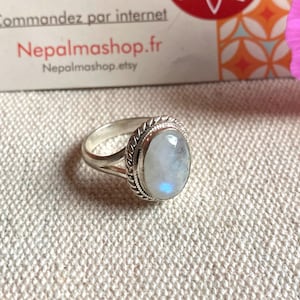 Peut inclure: Une bague en argent ornée d'une pierre de lune ovale en cabochon, entourée d'un bord en métal torsadé. L'anneau présente une conception fendue au niveau du sertissage, mettant en valeur une finition polie sur le métal et une pierre translucide.