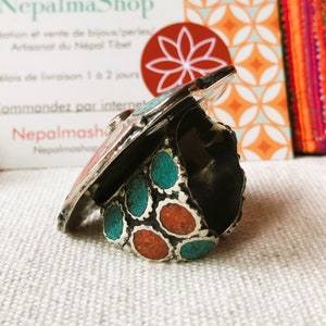 May include: A silver ring with turquoise and coral stones. The ring is set on a white fabric background.