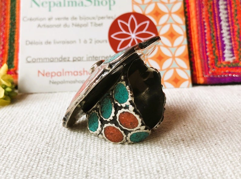 May include: A silver ring with turquoise and coral stones. The ring is set on a white fabric background.