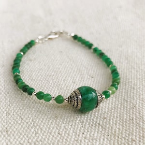 May include: A green gemstone bracelet with a silver clasp and a large green gemstone bead with silver accents.