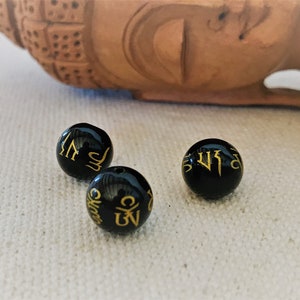 May include: Three black beads with gold lettering. The beads are round and have a smooth surface. The lettering on the beads is in a traditional style.