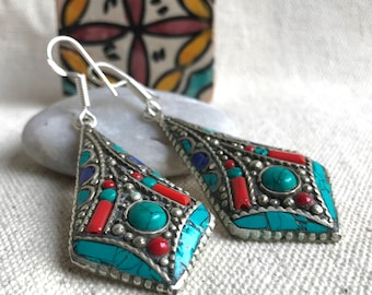 May include: A pair of silver dangle earrings featuring turquoise and coral stones. The earrings are shaped like a diamond and have a silver hook.