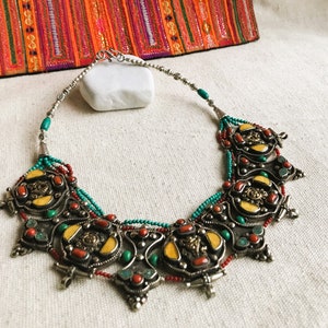 May include: A silver necklace with turquoise, red coral, and yellow stones. The necklace has a decorative design with intricate details.