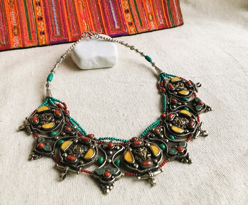 May include: A silver necklace with turquoise, red coral, and yellow stones. The necklace has a decorative design with intricate details.