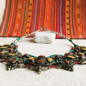 May include: A silver necklace with turquoise, coral, and yellow stones. The necklace is made of beads and has a pendant in the center.