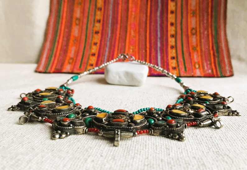 May include: A silver necklace with turquoise, coral, and yellow stones. The necklace is made of beads and has a pendant in the center.