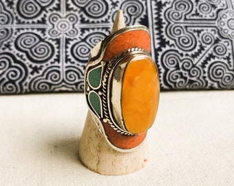 Könnte beinhalten: Ein silberner Ring mit einem orangefarbenen und grünen Steinbesatz. Der Ring befindet sich auf einem Holzständer.