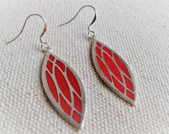 May include: A pair of silver earrings with red geometric designs. The earrings are shaped like a teardrop and have a silver hook.