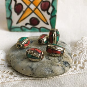 May include: Five oval-shaped beads with a gold metal base and red and green accents. The beads are arranged on a gray stone.