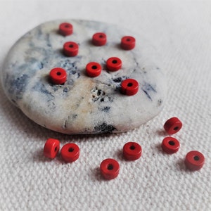 Peut inclure: Un ensemble de perles en bois rouge, certaines sur un rocher gris clair et d'autres éparpillées sur une surface en tissu blanc.