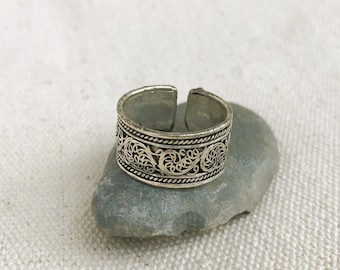 May include: A silver adjustable ring with an ornate openwork design. The ring showcases a detailed pattern of swirling floral and scroll motifs, giving a vintage or bohemian feel. The band is open, allowing for size adjustment.