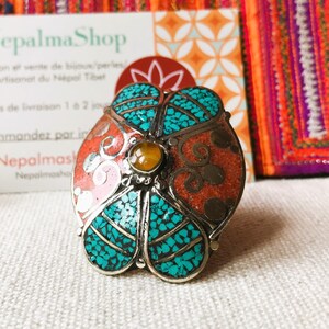 May include: A silver ring with a turquoise and coral inlay design. The ring is round and has a flower-like shape. The center of the ring has a small amber stone.