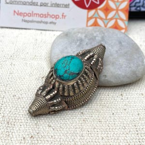May include: A silver pendant featuring a turquoise stone set in the centre. The pendant is decorated with intricate silver designs.