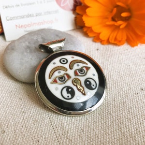 Op de afbeelding: Zilveren hanger met een zwart-wit emaille ontwerp met twee ogen, een yin yang symbool en andere geometrische vormen. De hanger is rond en heeft een zilveren lus.