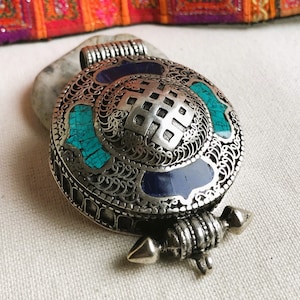 May include: Silver pendant with intricate filigree design and turquoise and blue enamel accents. The pendant features a traditional Tibetan knot symbol.