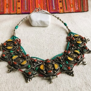 May include: A silver necklace with a large, ornate pendant featuring turquoise, coral, and yellow stones. The pendant is made up of several interlocking pieces, each with a different design. The necklace is a statement piece that would be perfect for a special occasion.