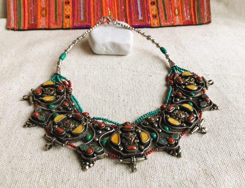 May include: A silver necklace with a large, ornate pendant featuring turquoise, coral, and yellow stones. The pendant is made up of several interlocking pieces, each with a different design. The necklace is a statement piece that would be perfect for a special occasion.