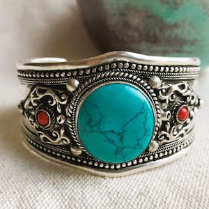 Peut inclure: Bracelet en argent avec une pierre turquoise et des accents de corail rouge. Le bracelet a un design complexe avec une bordure perlée.
