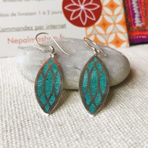 May include: A pair of silver-toned earrings with a leaf-like shape. Each earring features a teal glitter-filled design within a silver frame. The earrings are displayed on a white surface.
