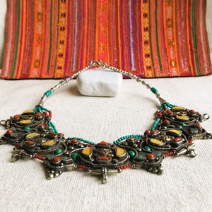 May include: A silver necklace with turquoise, red coral, and yellow stones. The necklace has a decorative, ornate design with multiple pendants.