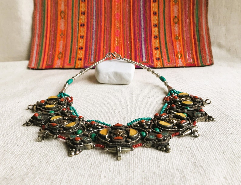 May include: A silver necklace with turquoise, red coral, and yellow stones. The necklace has a decorative, ornate design with multiple pendants.