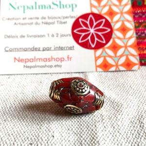 Könnte beinhalten: Eine rote Korallenperle mit goldenen Akzenten und einem kleinen roten Stein in der Mitte. Die Perle ist etwa 2,5 cm lang.
