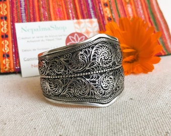 May include: A silver bracelet featuring an elaborate floral design. The bracelet is wide and curved, crafted from filigree, a delicate and intricate metalwork technique.