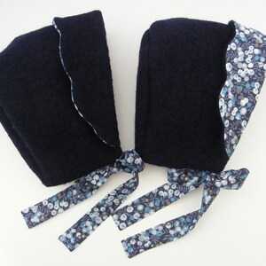 Peut inclure: Deux bonnets bleu marine avec une bordure à motifs floraux et des liens assortis. Les bonnets ont une forme arrondie et sont faits d'un tissu doux et texturé. Le motif floral présente des baies bleues et blanches sur fond marine.