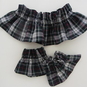 Könnte beinhalten: Drei Stoffstücke mit einem schwarz-weiß-roten Karomuster. Der Stoff ist gerafft und gerüscht, möglicherweise für Kleidung oder Accessoires. Die Teile sind wahrscheinlich dekorativ.