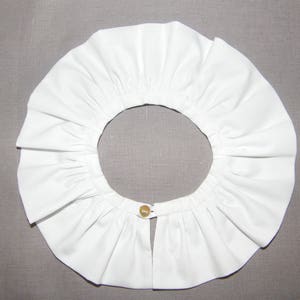 Peut inclure: Un col blanc à volants avec une fermeture à bouton unique au centre.