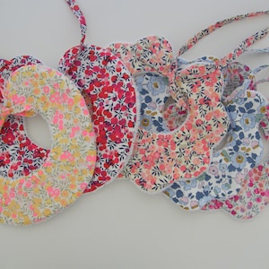 Peut inclure: Un ensemble de six bavoirs en coton à imprimé floral coloré avec des bords festonnés et des liens. Les bavoirs sont en tissu de coton et présentent une variété de motifs floraux dans des tons de rose, rouge, bleu et jaune.