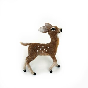 The picture shows a beautiful wool, needle felted toy fawn standing on a palm, the background is white.