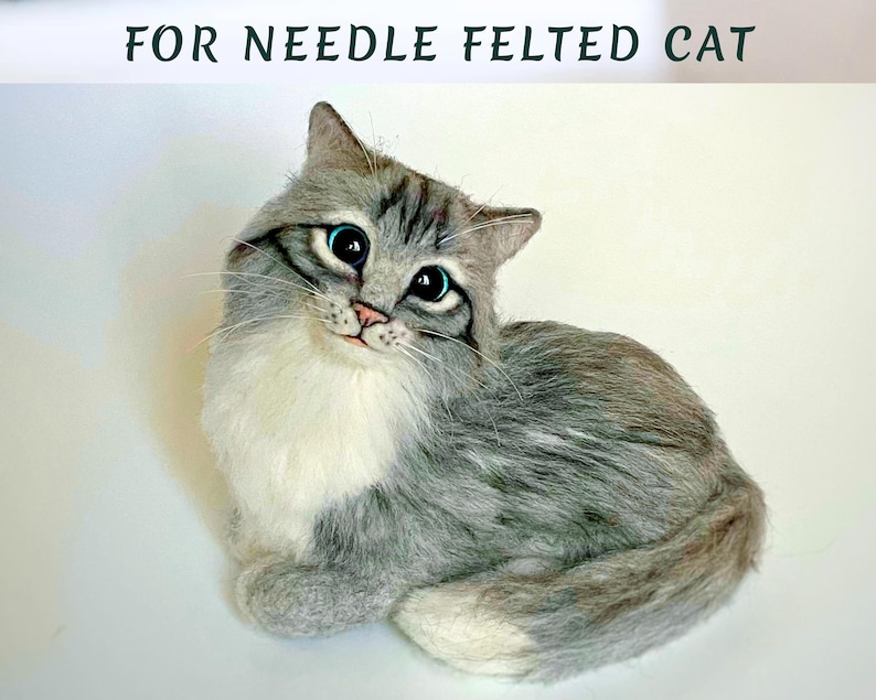 Pode incluir: Figura de gato em feltro com agulha, com pelo cinza e branco, olhos azuis grandes e nariz rosa. O gato est&aacute; sentado com a cabe&ccedil;a ligeiramente inclinada. O texto na parte superior diz "FOR NEEDLE FELTED CAT."