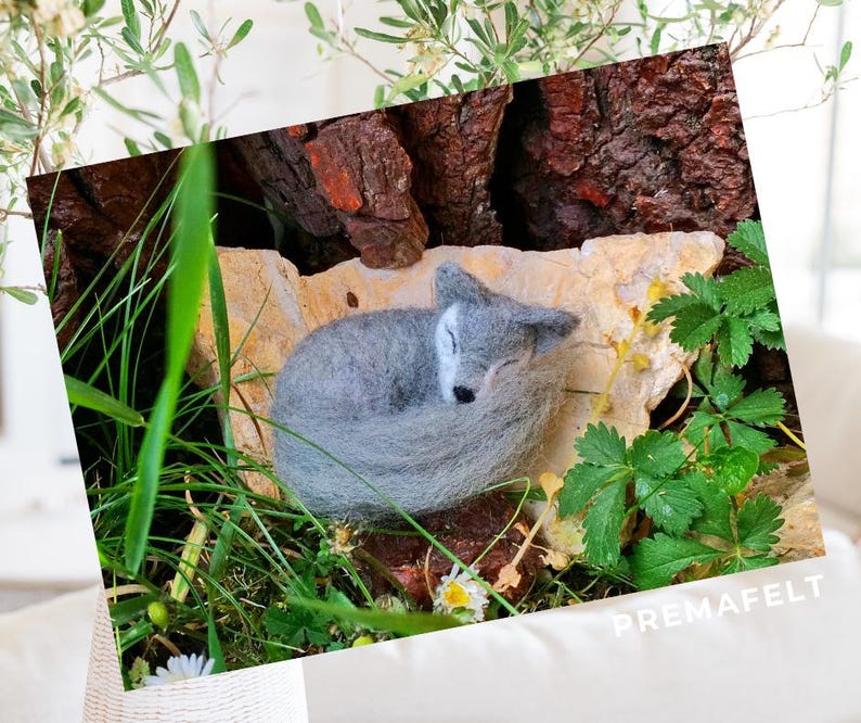 In the picture, a fluffy wool toy little wolf is lying curled up in the green grass.