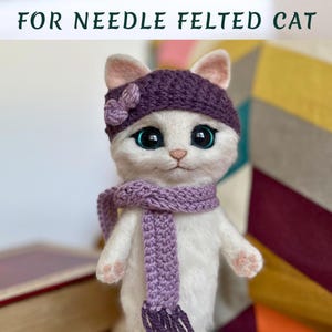 Pode incluir: Uma boneca de gato branca de feltro com agulha, usando um chap&eacute;u de malha roxo com um detalhe de flor e um cachecol a condizer. O gato tem olhos grandes e expressivos e orelhas e patas cor-de-rosa. O texto "FOR NEEDLE FELTED CAT" est&aacute; no topo.