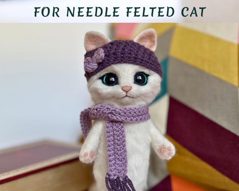 Pode incluir: Uma boneca de gato branca de feltro com agulha, usando um chap&eacute;u de malha roxo com um detalhe de flor e um cachecol a condizer. O gato tem olhos grandes e expressivos e orelhas e patas cor-de-rosa. O texto "FOR NEEDLE FELTED CAT" est&aacute; no topo.