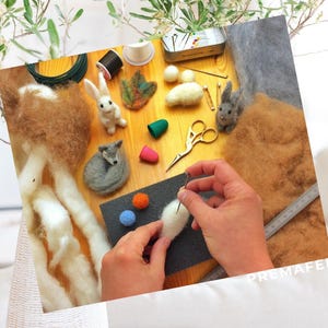 The picture shows a little wolf made of wool being made with needle felting, with wool and accessories in the background.