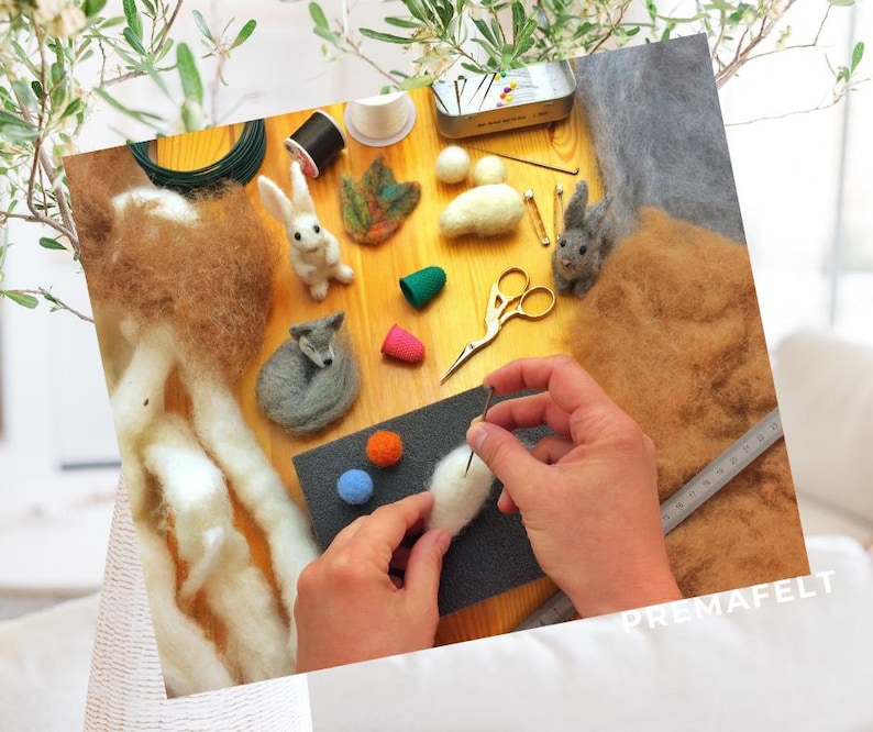 The picture shows a little wolf made of wool being made with needle felting, with wool and accessories in the background.