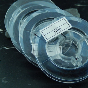 Peut inclure: Bobines de fil noir en plastique transparent, chacune avec une étiquette indiquant "10m".