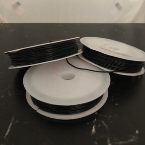 May include: Three spools of black elastic cord, each wound around a white plastic spool.