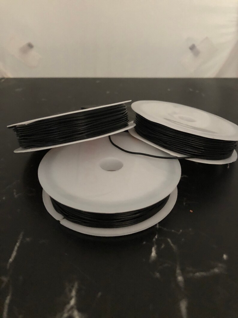 May include: Three spools of black elastic cord, each wound around a white plastic spool.