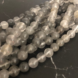 Könnte beinhalten: Eine Strähne aus grauen und klaren runden Edelsteinperlen. Die Perlen sind glatt und durchscheinend, mit einem leichten Schimmer.