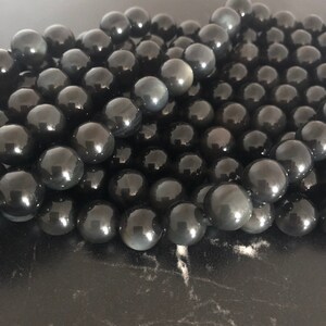 Peut inclure: Gros plan sur un tas de perles d'obsidienne noire. Les perles sont rondes et lisses, et elles ont un léger éclat.