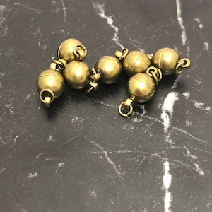 Può includere: Un gruppo di sei perline in metallo dorato con anelli. Le perline sono collegate tra loro da piccoli anelli in metallo.